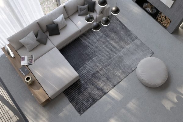 Stylish Kymo rug under a modern sofa and round pouf – softly angled view.