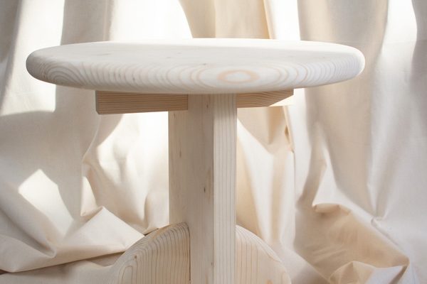 Round natural wood side table placed on a soft fabric background – minimalist design accent.