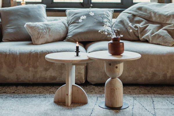 Two round wooden side tables with candle and vase in front of a beige corduroy sofa – NIROH interior accent