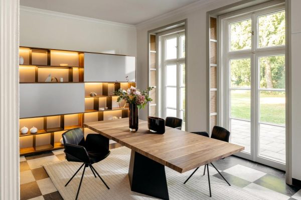 Rodam dining setup with central pedestal table, three black leather chairs and illuminated wall unit – modern elegance in detail.