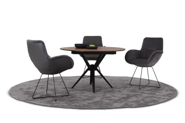 Three Werther fabric-upholstered chairs around a round table, placed on a gray circular rug – inviting dining corner.