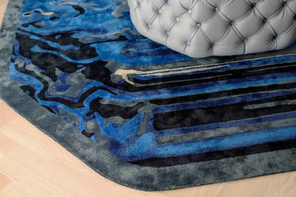 Close-up of blue designer carpet with abstract linear and organic shapes, combining dark navy, teal, and grey tones.
