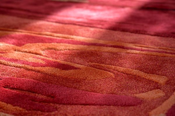 Macro shot of red carpet texture showing layered surface details in shades of orange, coral, and crimson.