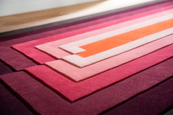 Detail shot of carpet runner with raised surface levels and linear gradient from coral to plum tones.