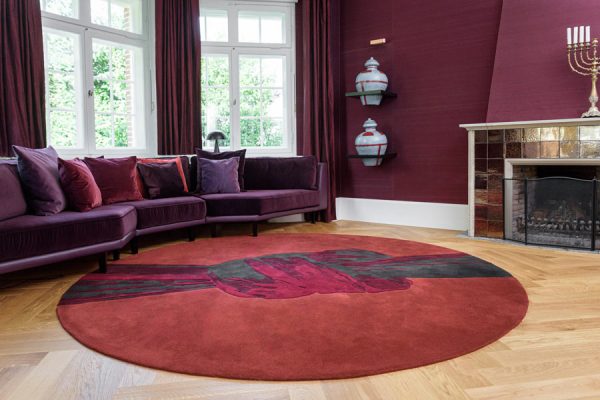 Living room scene with round red designer carpet featuring abstract black and purple overlay, paired with velvet seating – from the 'Daydreams' collection.