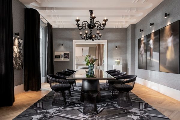 Elegant dining room with a rectangular table and black chandelier, featuring a monochrome designer rug showing detailed intertwined hands.