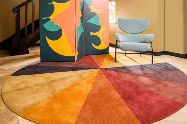 Vibrant room with multicolor circular rug in warm tones, paired with an artistic folding screen and modern chair.