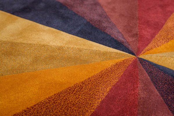Detail of multicolor rug showing textured wedge-like segments in bold orange, red, and purple hues.