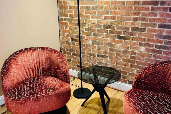 518 North showroom – lounge corner featuring two Werther accent chairs, a Holtkötter floor lamp and a round Rodam glass side table set against an exposed brick wall