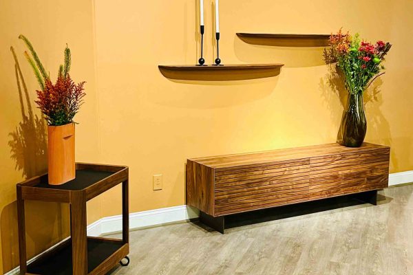 518 North showroom – Rodam wooden sideboard and matching rolling cart with floral decor, set against warm yellow walls with minimalist floating shelve